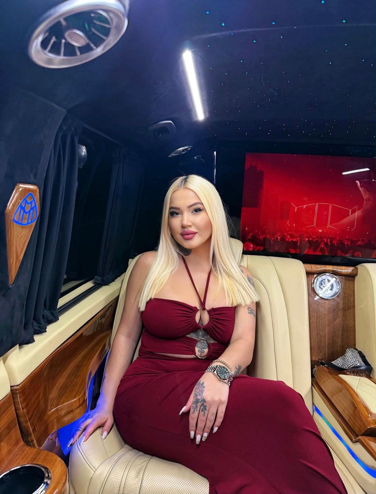 Woman with long blond hair in a burgundy dress sits in a luxury limo with a starry ceiling.