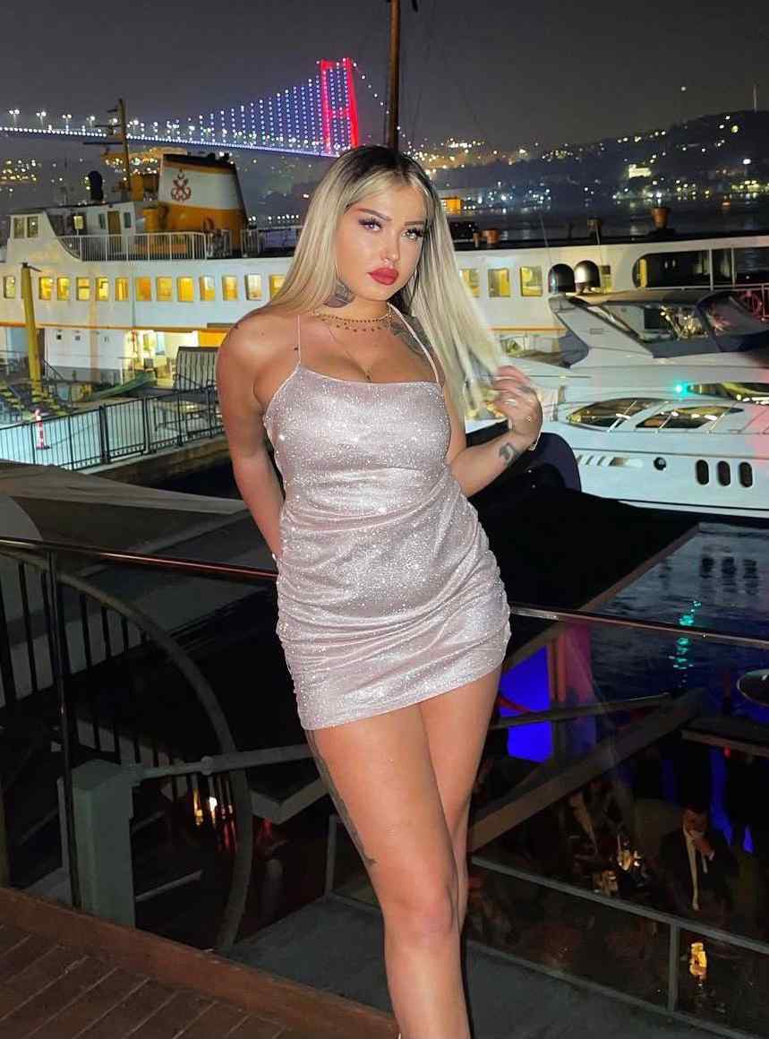 Woman in a sparkly silver dress posing on a marina deck at night with boats and city lights behind her