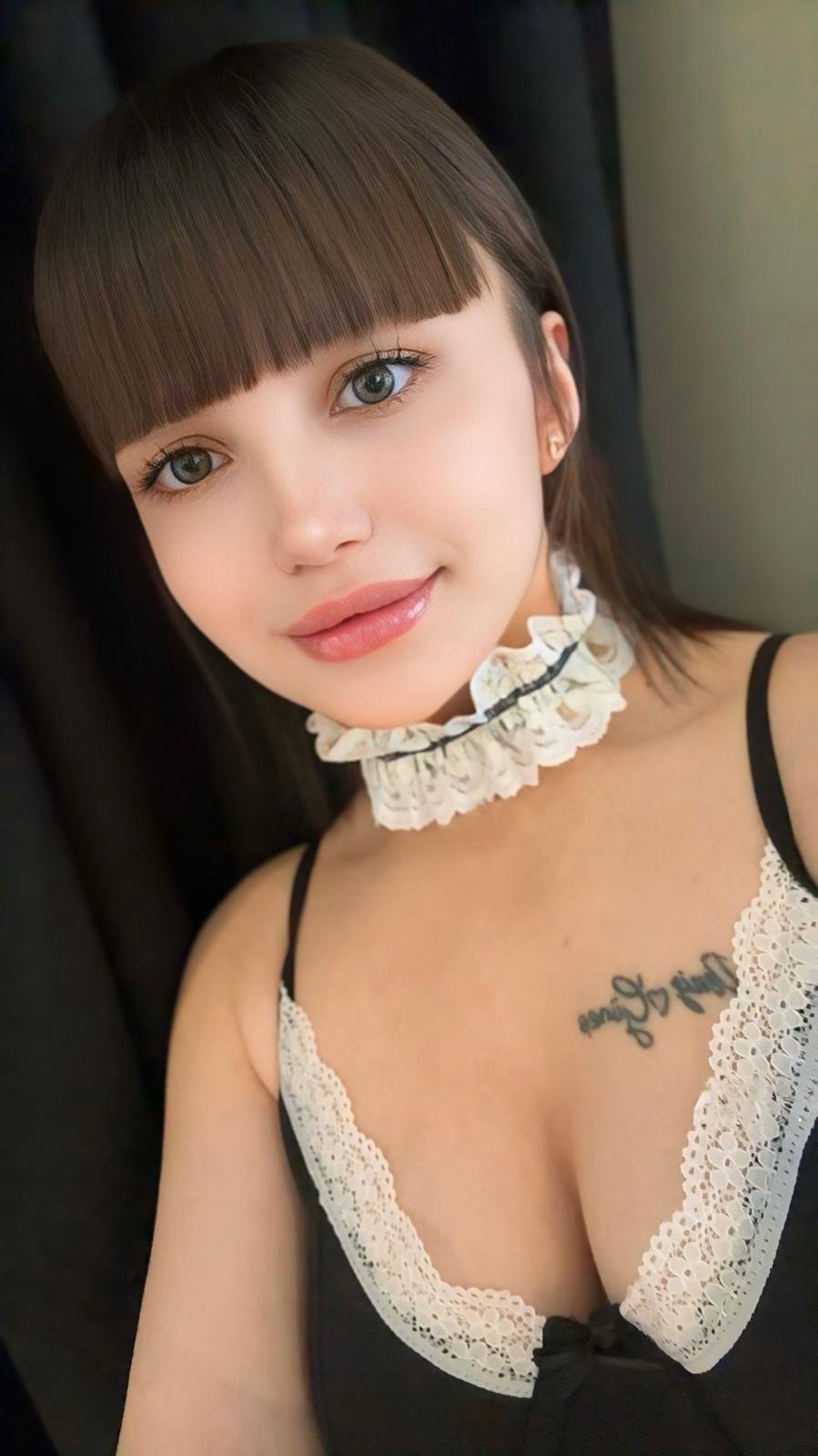 Close-up portrait of a young woman with brown bangs, wearing a white lace choker and black lace-trimmed top.