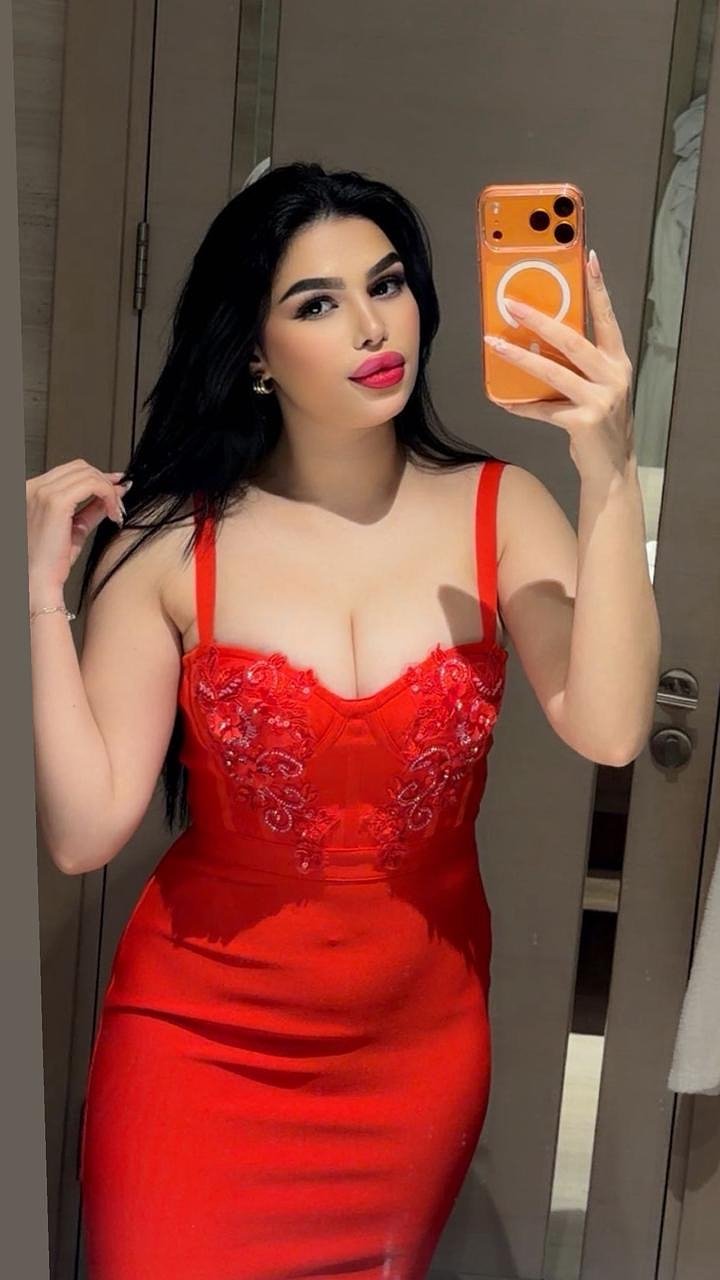 Woman takes a mirror selfie in a red satin dress with lace embroidery, holding an orange phone.