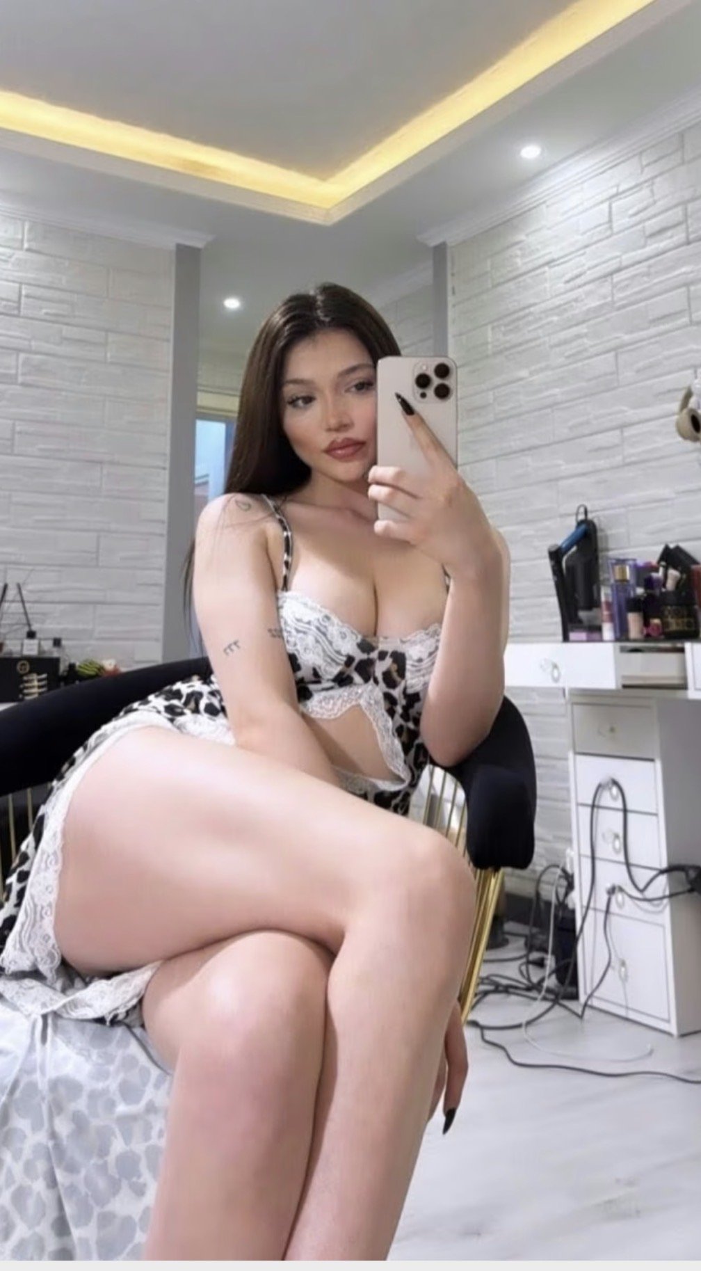 woman in white lace lingerie posing for a mirror selfie in a bright, modern bedroom, holding a smartphone
