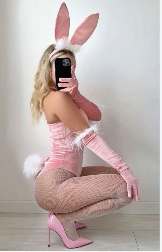 Person in a pink bunny costume with ears, fluffy tail, gloves, and pink high heels posing for a mirror selfie.