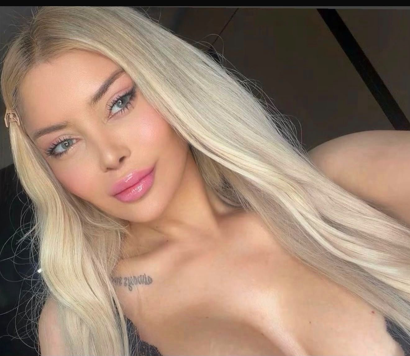Close-up selfie of a young woman with long platinum-blonde hair, blue eyes, pink lips, and subtle makeup.