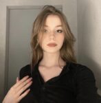 Young woman with light brown hair wearing a black shirt, looking at the camera with a neutral expression.