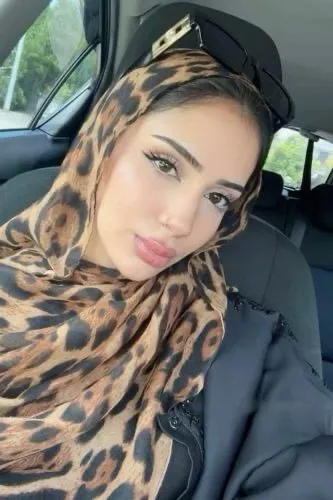 Woman in a leopard-print hijab in a car, looking at the camera with a neutral expression.
